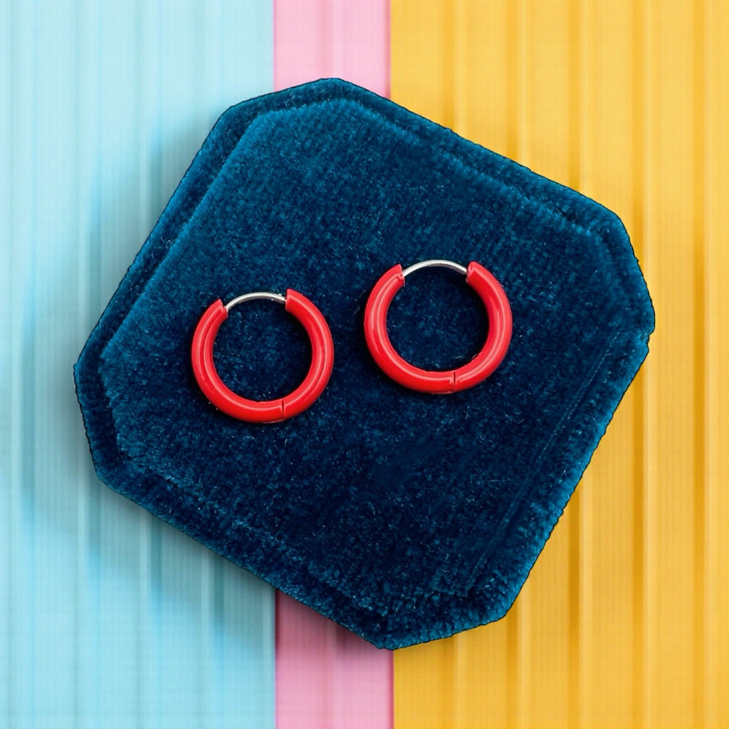 Red hoop earrings on a blue hexagonal velvet stand against a colorful background