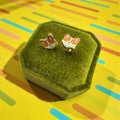 Corgi-shaped earrings in a green box on a colorful background