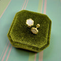 Gold earrings with a white center on a green velvet jewelry box against a striped background