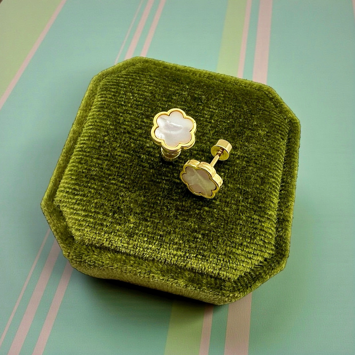 Gold earrings with a white center on a green velvet jewelry box against a striped background